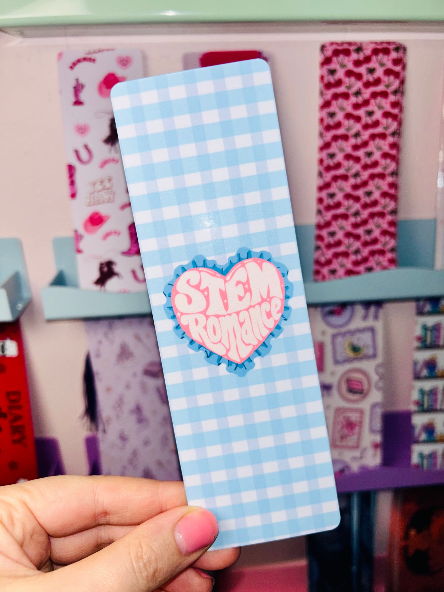 Double-sided science romance bookmark, blue check front with pink heart badge, held in hand