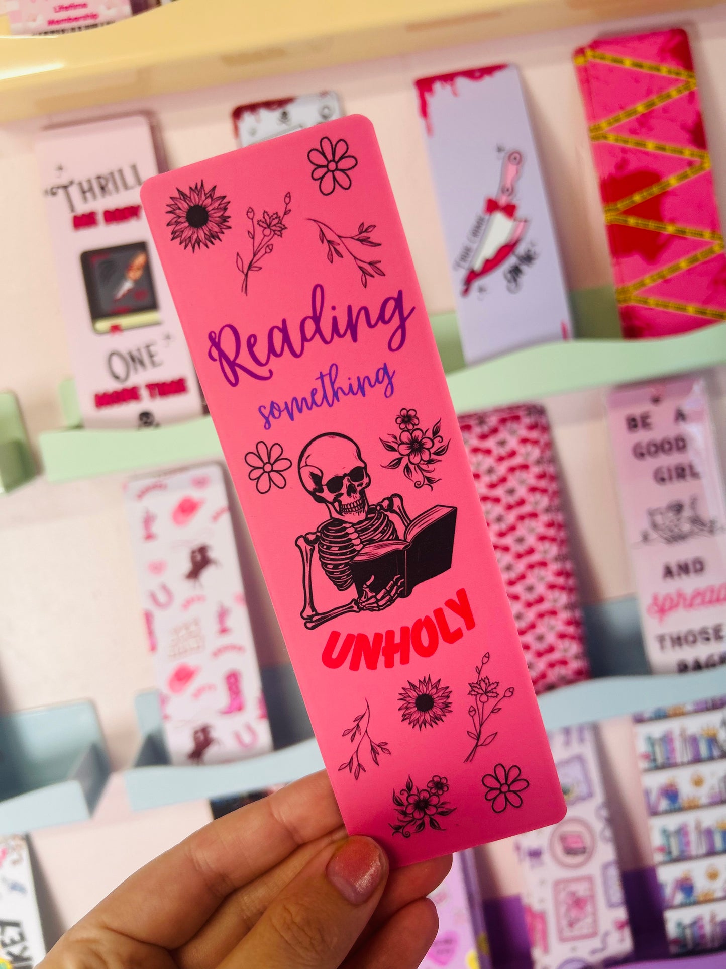 Pink bookmark held up, "Reading something" and "UNHOLY" with black skeleton and flowers