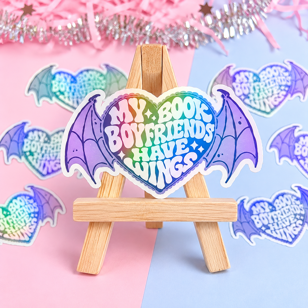 Holographic bat-wing sticker with “Book Boyfriends Have Wings” text on small wooden easel