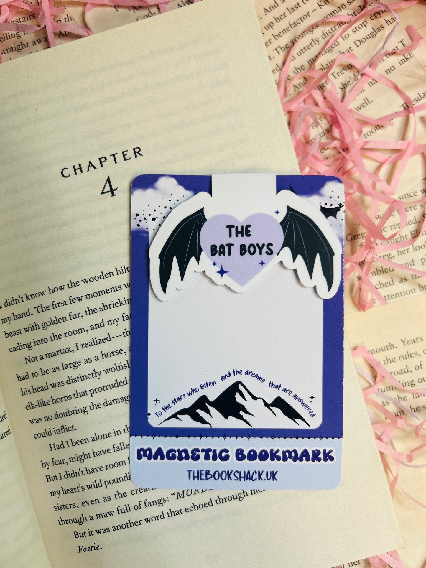 Magnetic bookmark featuring a purple heart with the text “The Bat Boys,” flanked by bat wings, clipped to an open fantasy book.