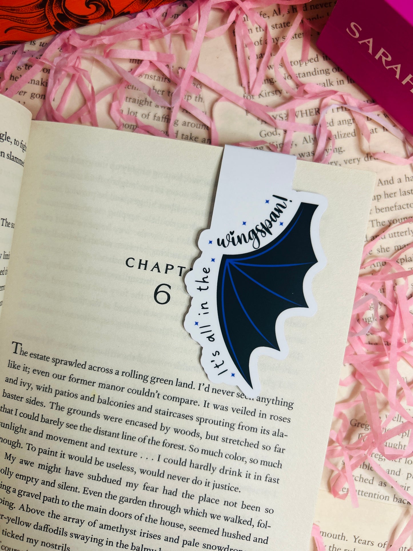 Magnetic bat wing bookmark with the phrase “It’s All in the Wingspan,” clipped to an open book with a fantasy-themed background.