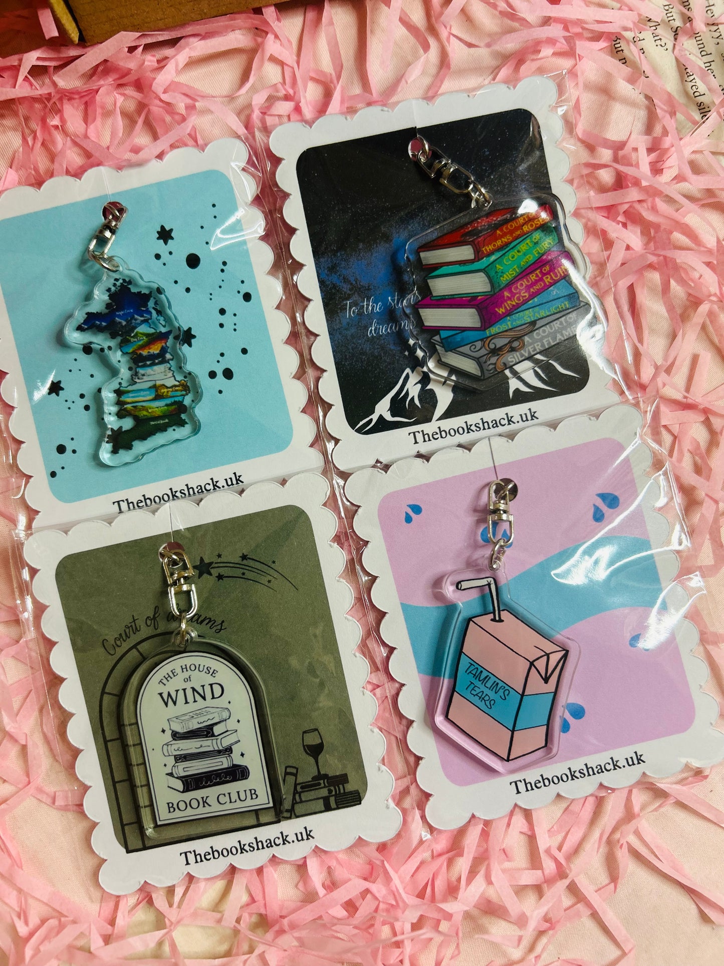 Flat lay of an ACOTAR-themed mystery bookish bundle featuring double-sided bookmarks, holographic stickers, a keyring, art print, annotate tabs, pen and highlighter. Items are displayed with Sarah J. Maas books and pink shredded paper, creating a cosy, fantasy-inspired aesthetic.