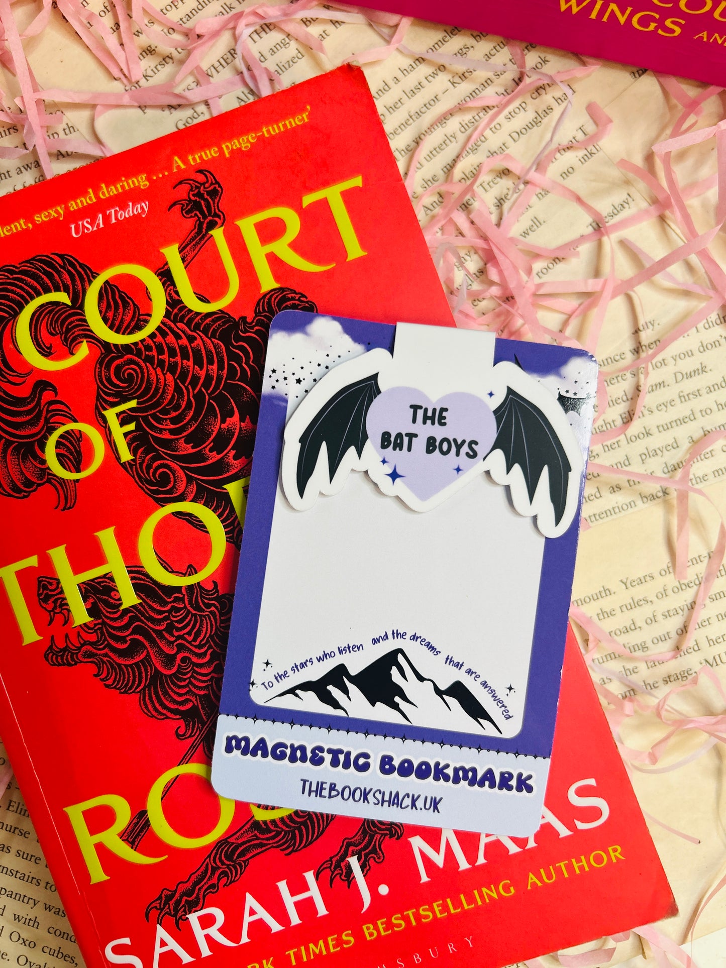 Magnetic bookmark featuring a purple heart with the text “The Bat Boys,” flanked by bat wings, clipped to an open fantasy book.