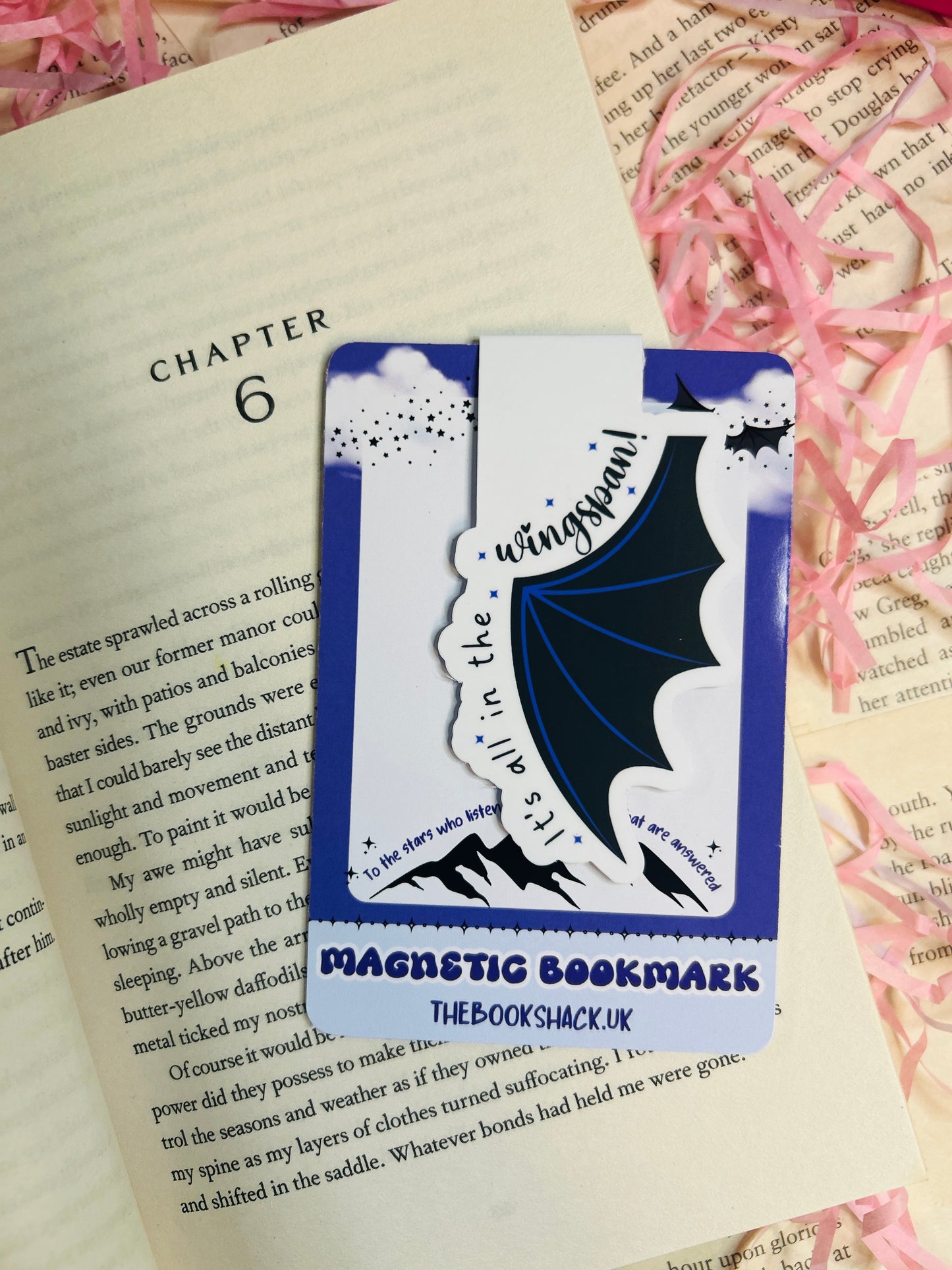 Magnetic bat wing bookmark with the phrase “It’s All in the Wingspan,” clipped to an open book with a fantasy-themed background.