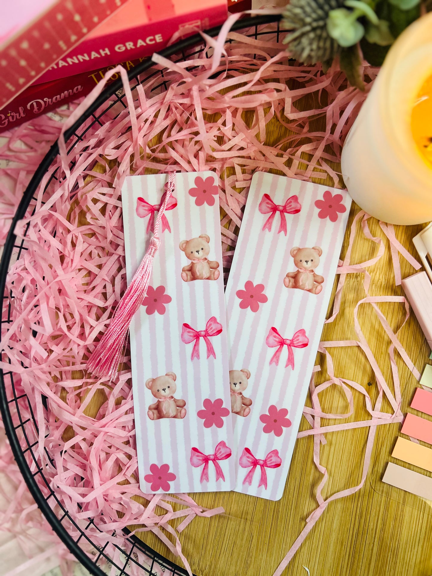 A pink teddy bear-themed bookmark with soft vertical stripes, delicate bows, and floral details, featuring a matching pink tassel.