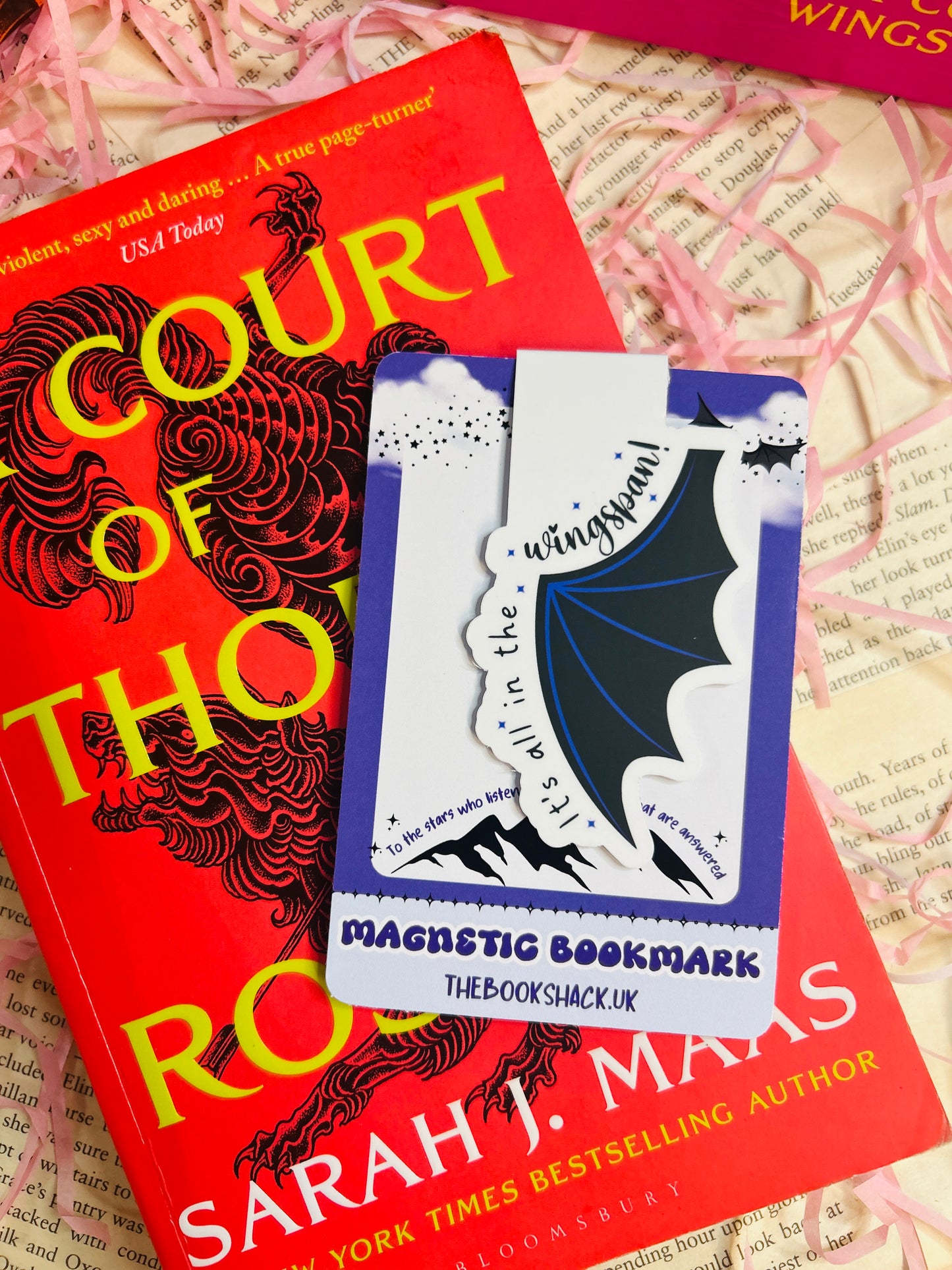 Magnetic bat wing bookmark with the phrase “It’s All in the Wingspan,” clipped to an open book with a fantasy-themed background.
