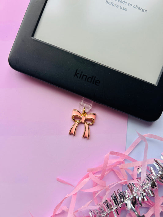 Pink bow Kindle charm attached to a clear plastic Type-C dust plug, displayed with backing card and holographic packaging, shown with optional white letter charm.