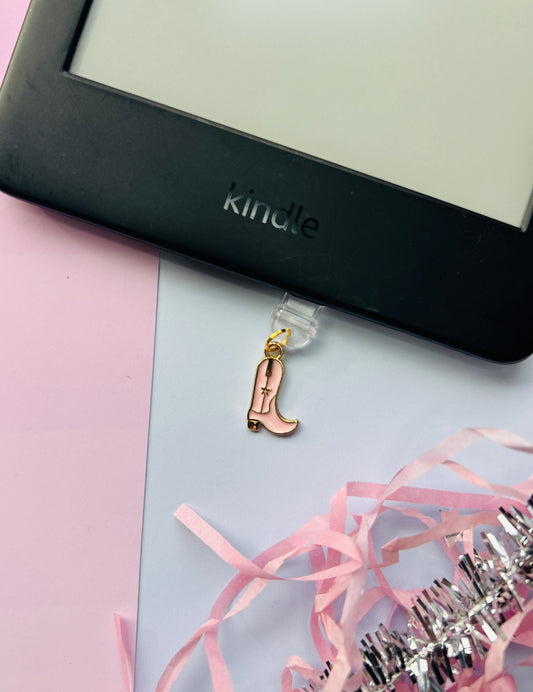 Pink cowboy boot Kindle charm attached to a clear plastic Type-C dust plug, shown with backing card and holographic packaging, plus optional white letter charm.