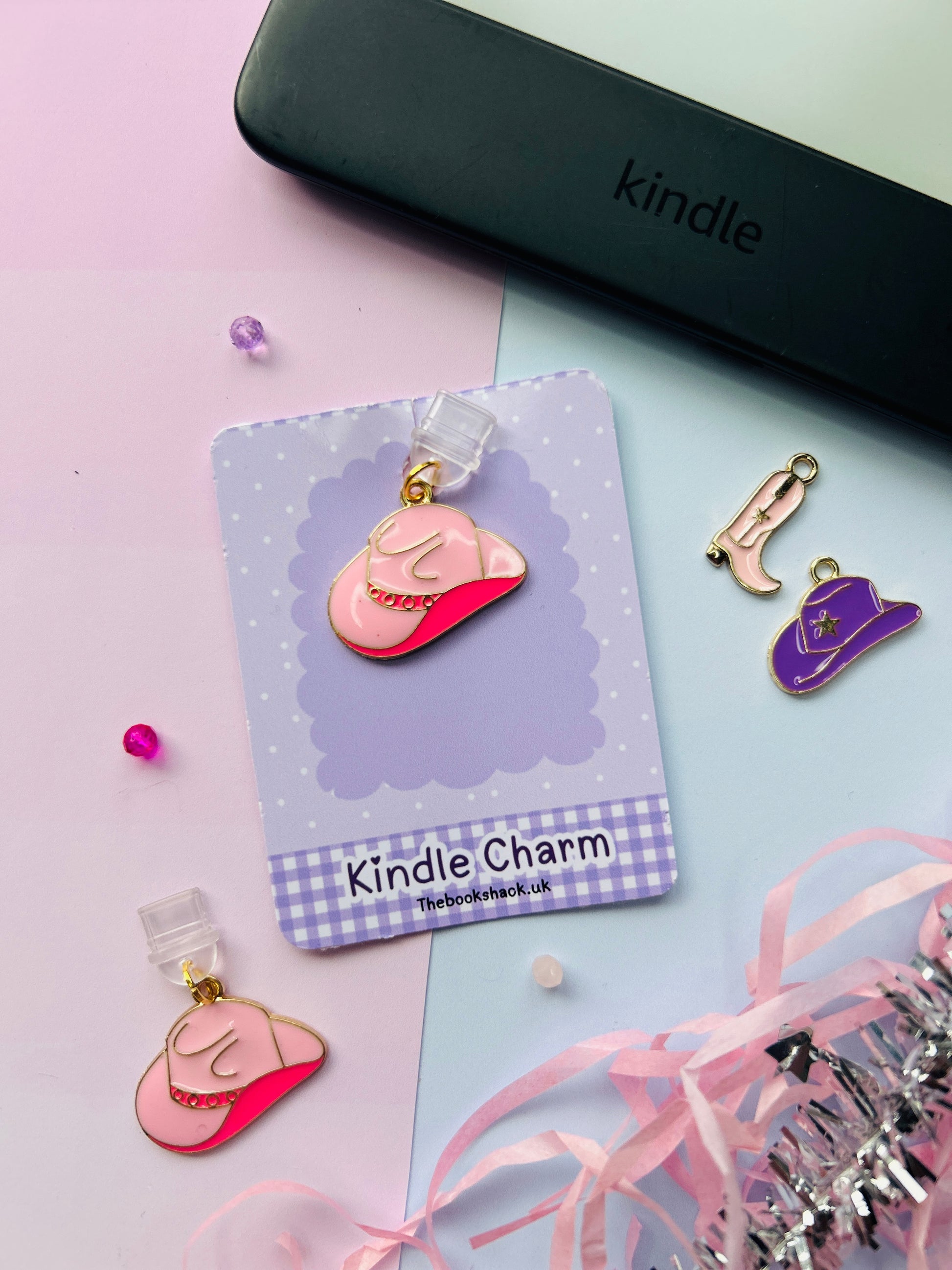 Pink cowboy hat Kindle charm attached to a clear plastic Type-C dust plug, packaged with backing card and holographic bag, shown with optional white letter charm.