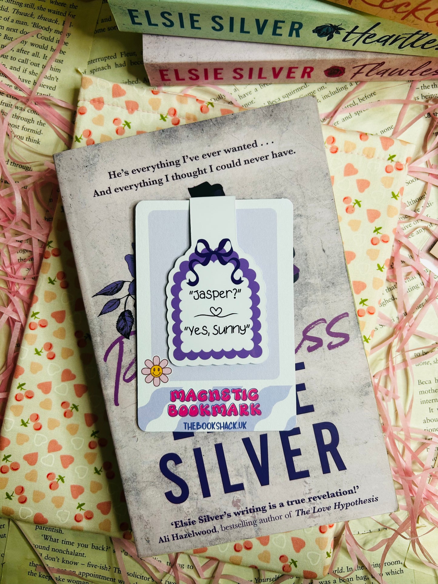 Magnetic bookmark featuring the quote 'Jasper? Yes, Sunny' with a purple scalloped edge and floral accent, placed on Elsie Silver's romance novel 'Flawless.'