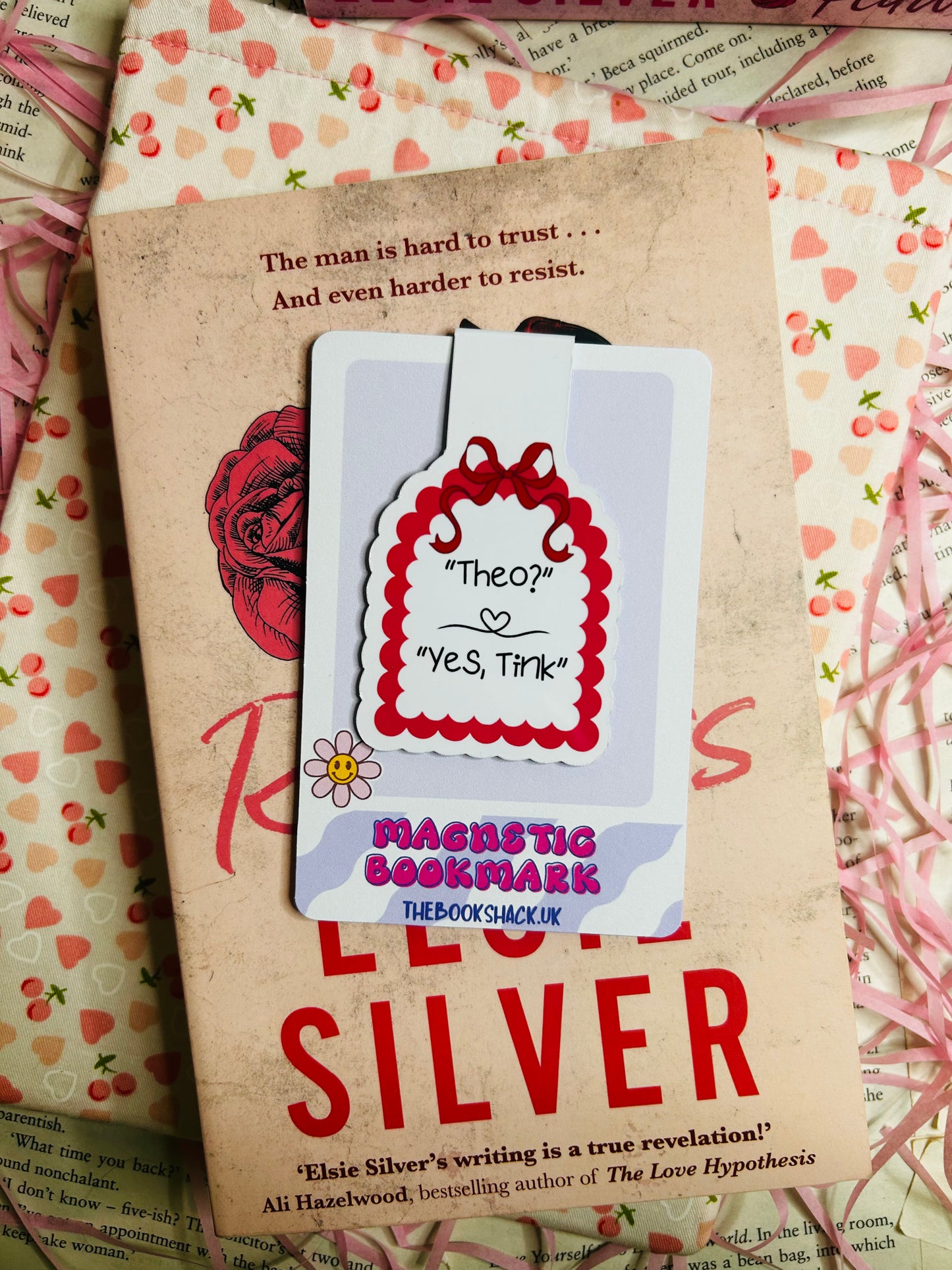 Magnetic bookmark featuring the quote 'Theo? Yes, Tink' with a red scalloped border and floral detail, resting on Elsie Silver's romance novel 'Reckless.'