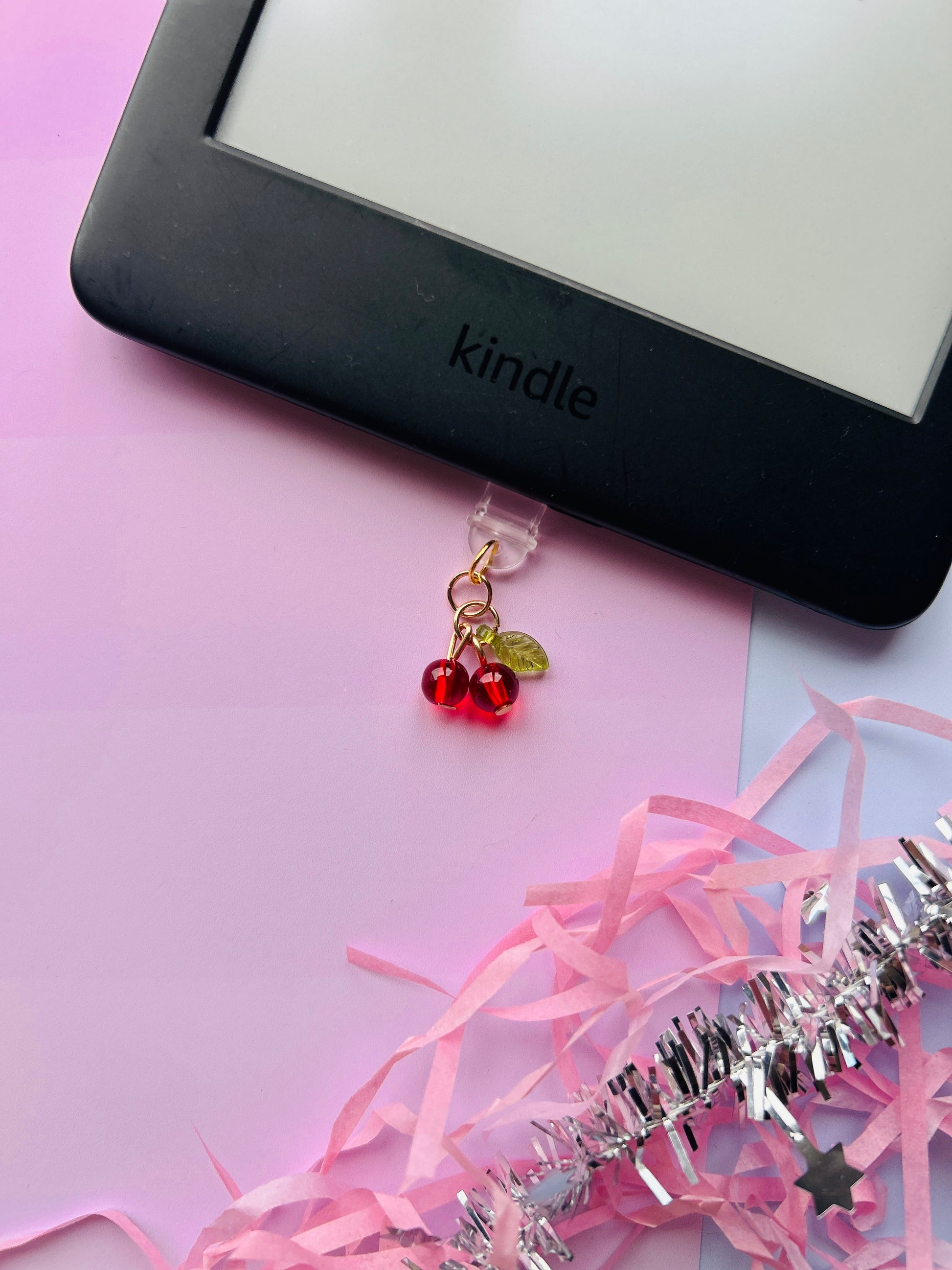 Cherry Kindle charm attached to a clear plastic Type-C dust plug, displayed with backing card and holographic packaging, with optional white letter charm.