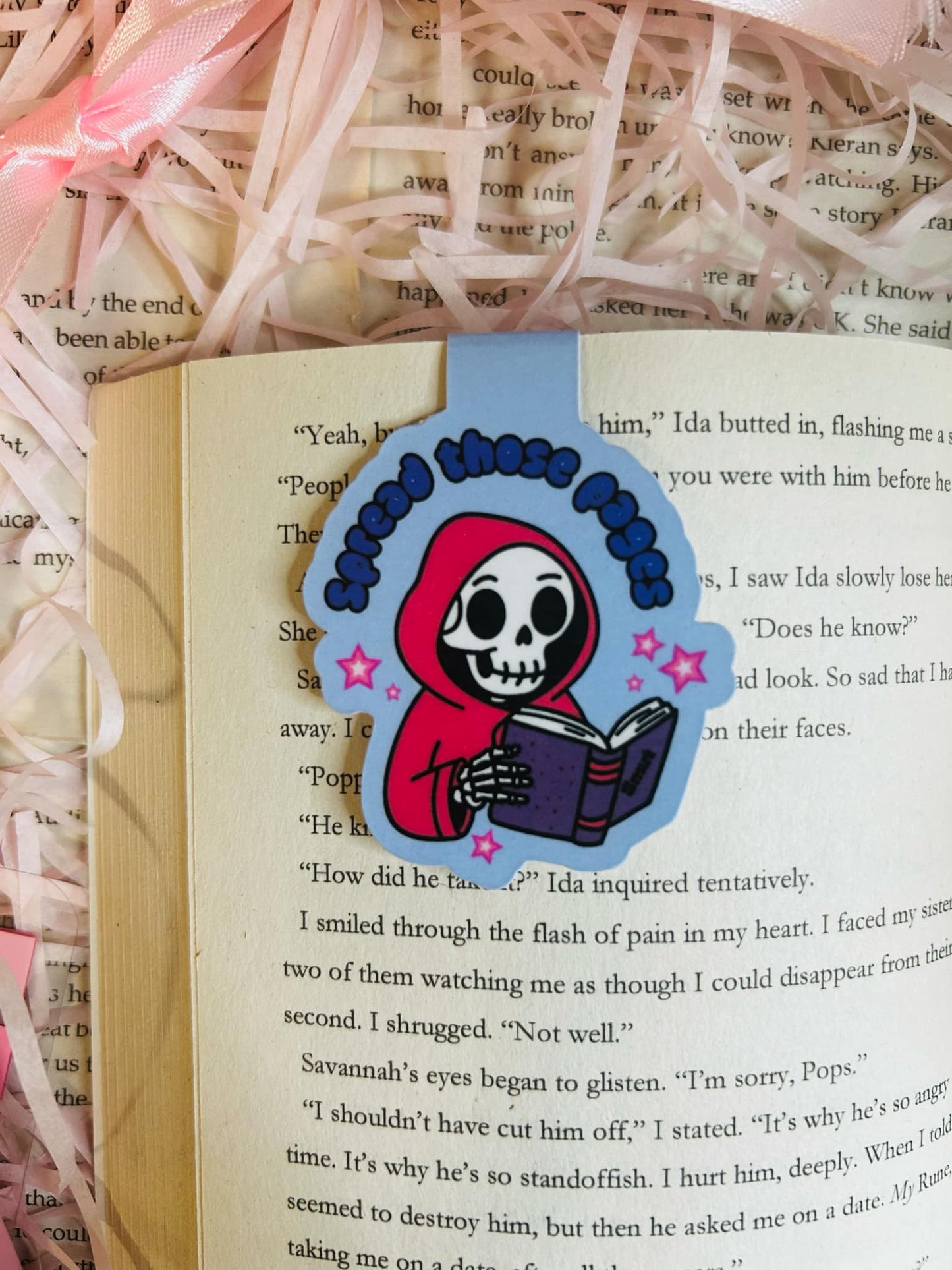 Magnetic bookmark featuring a cute skeleton in a red hoodie reading a book with the phrase 'Spread Those Pages,'