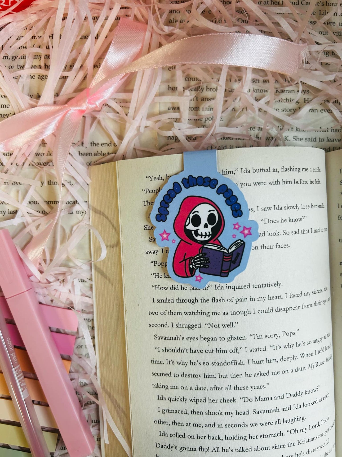 Magnetic bookmark featuring a cute skeleton in a red hoodie reading a book with the phrase 'Spread Those Pages,'
