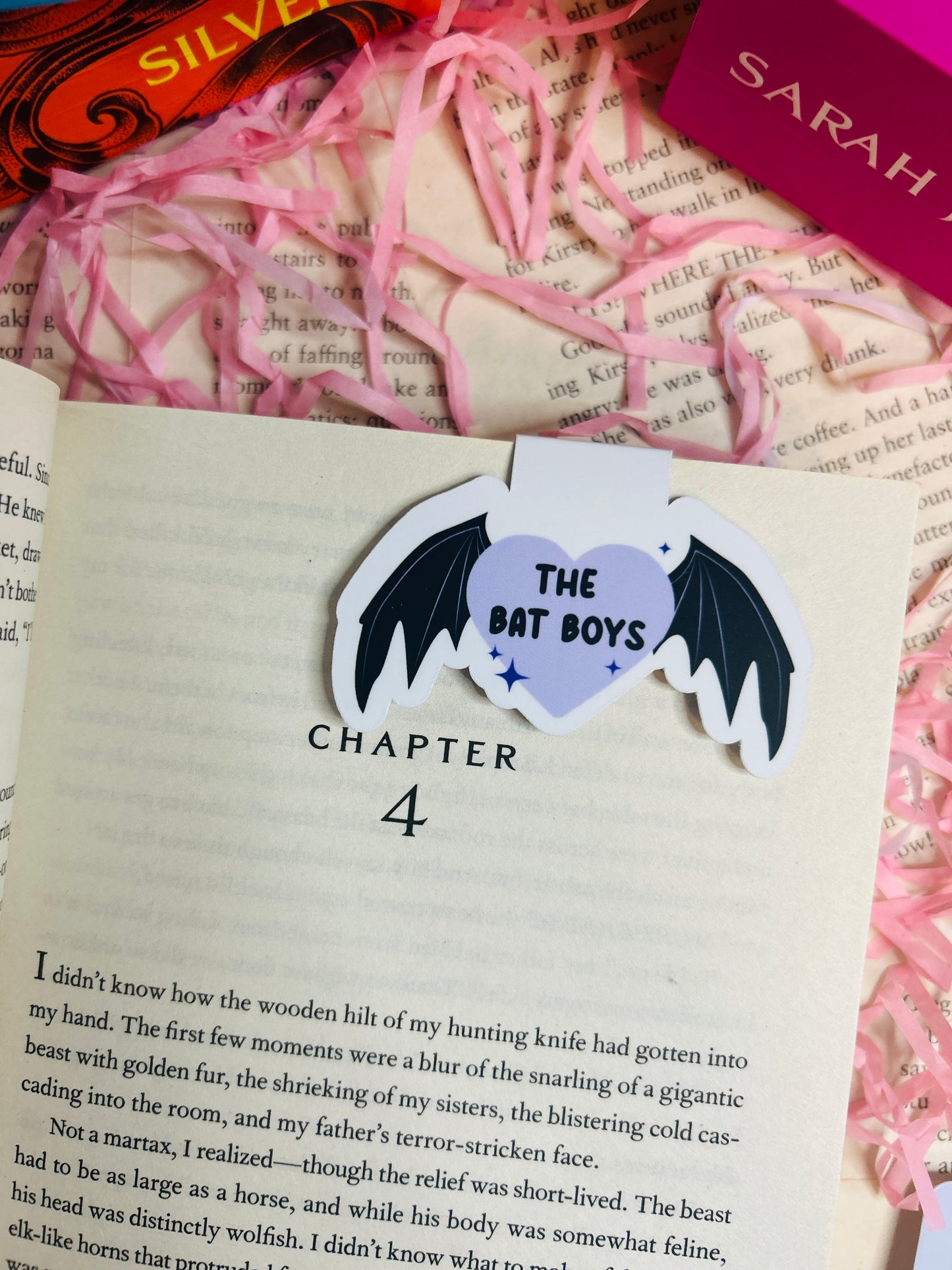 Heart-shaped sticker with bat design on a book page, surrounded by pink ribbons and a book titled 'Silver'.