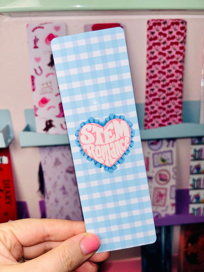 Double-sided science romance bookmark, blue check front with pink heart badge, held in hand