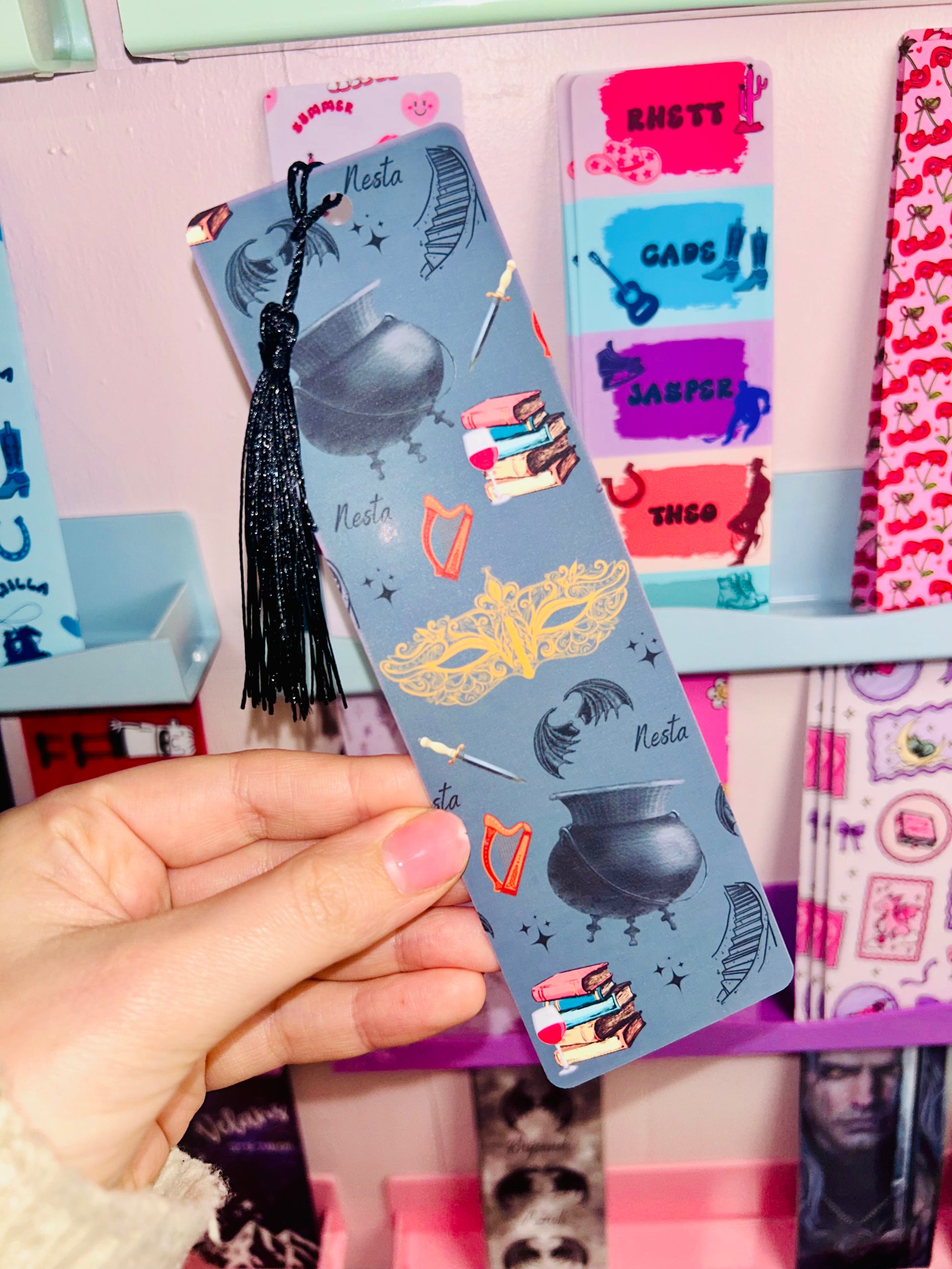 Illustrated bookmark in blue tones with black tassel, held in hand