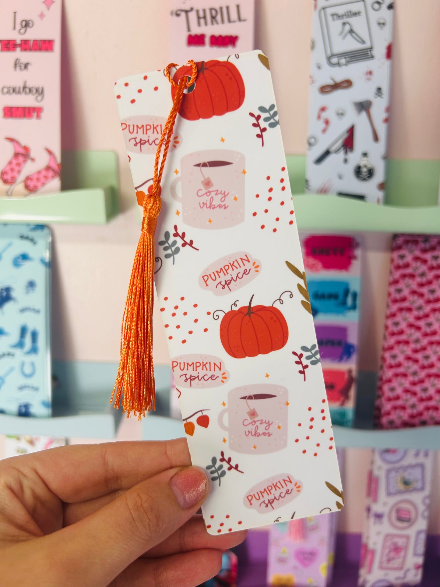 Hand holding an autumn pumpkin spice paper bookmark with orange tassel and pumpkin pattern