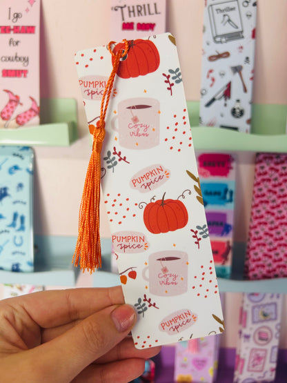 Hand holding an autumn pumpkin spice paper bookmark with orange tassel and pumpkin pattern