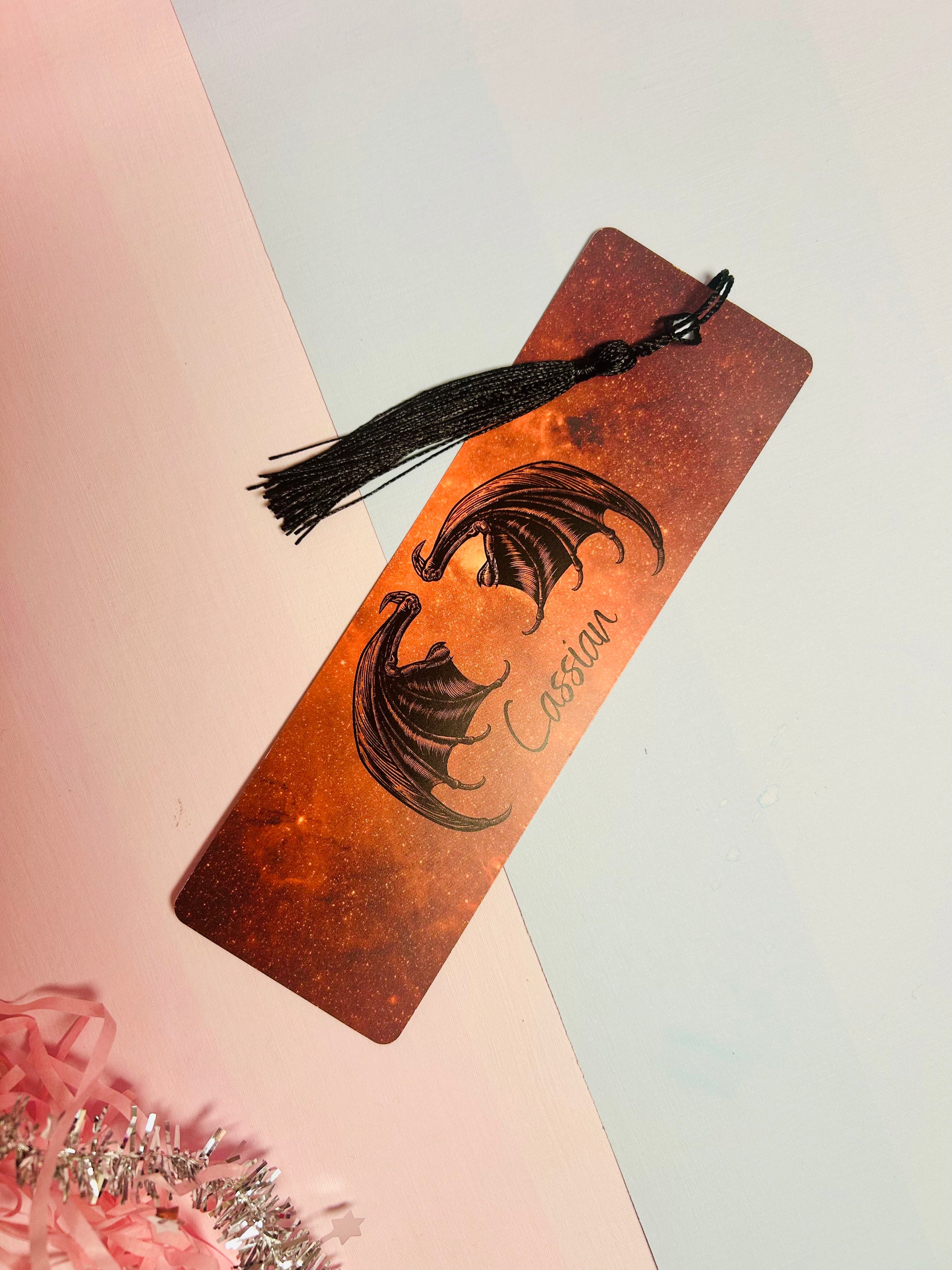 Orange glitter bookmark with face illustration and black tassel tied at top