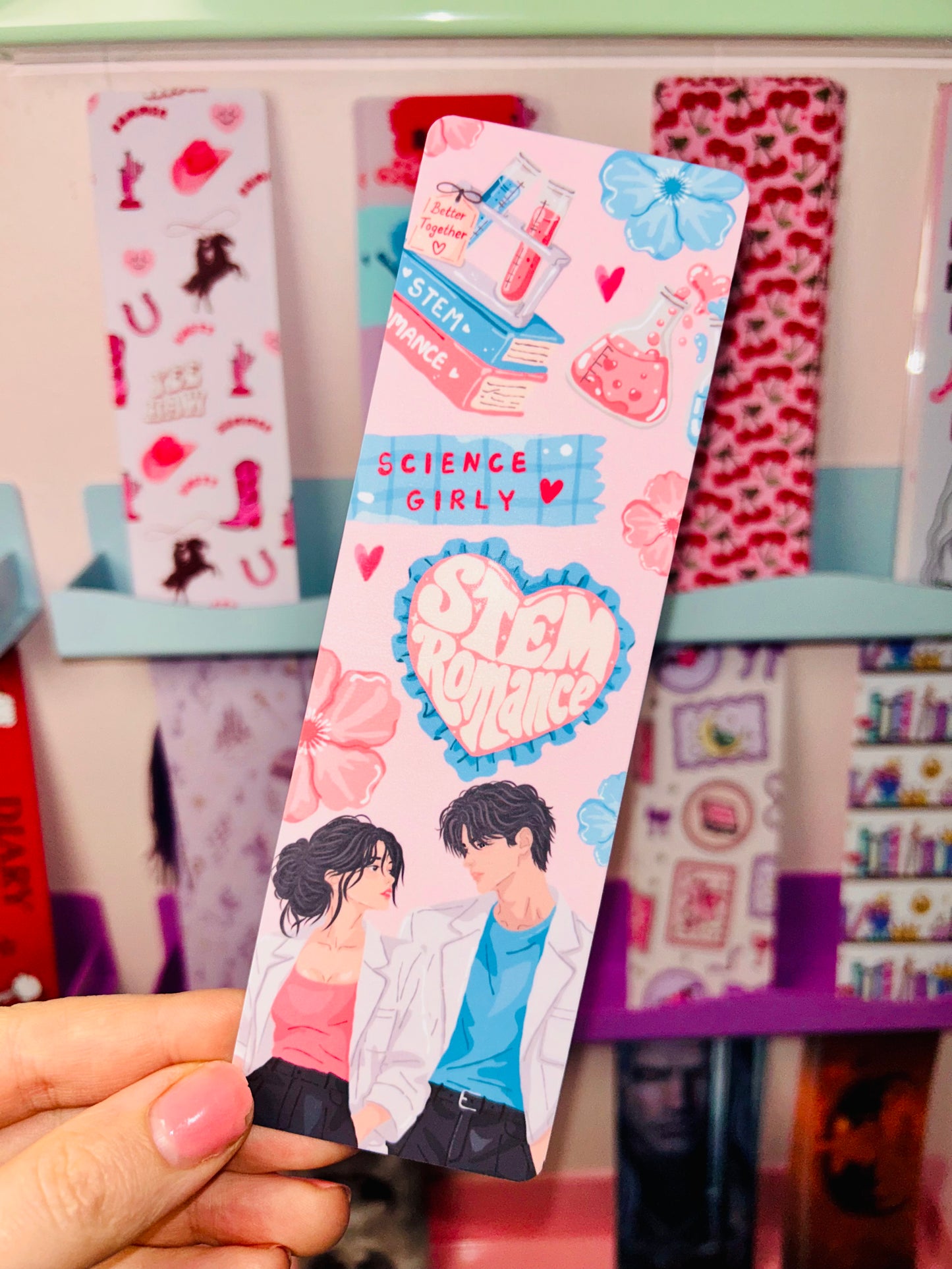 Science romance bookmark with blue heart bow top, held in hand