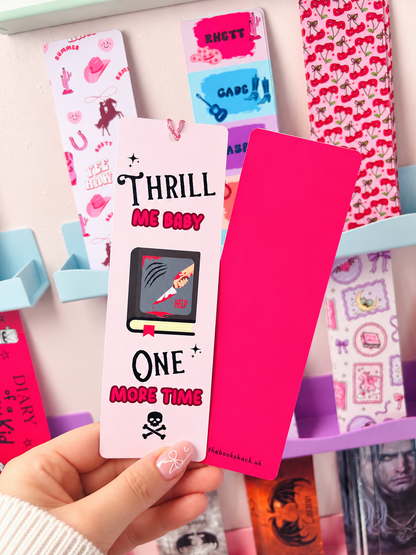 Pink tassel bookmark reading 'THRILL ME BABY' and 'ONE MORE TIME', held with another bookmark.