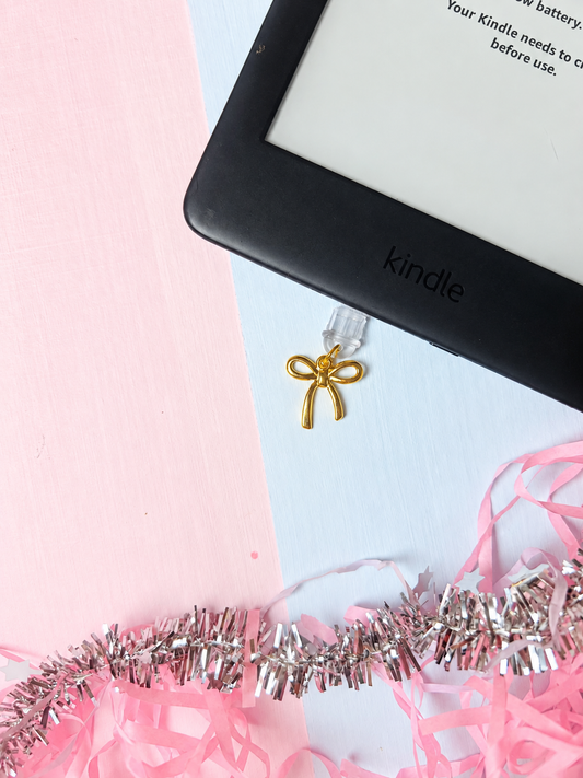 Gold bow USB-C dust plug charm near a black device port
