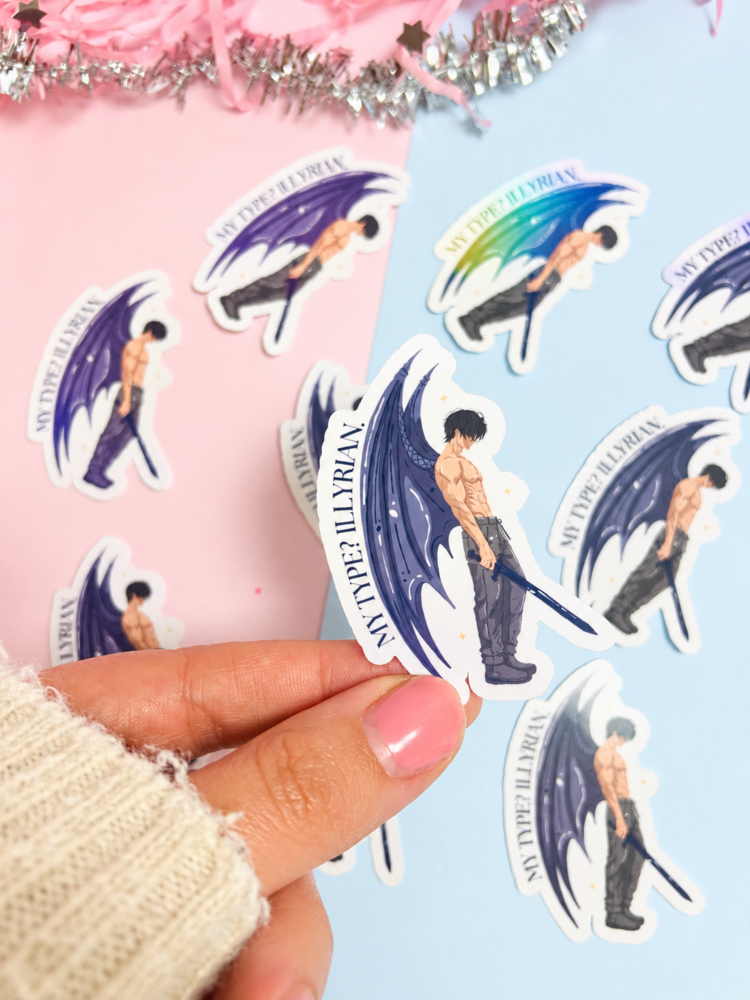 Holographic bat-boy character sticker with blue wings, circular text border, held by hand
