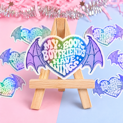 Holographic bat-wing sticker with “Book Boyfriends Have Wings” text on small wooden easel