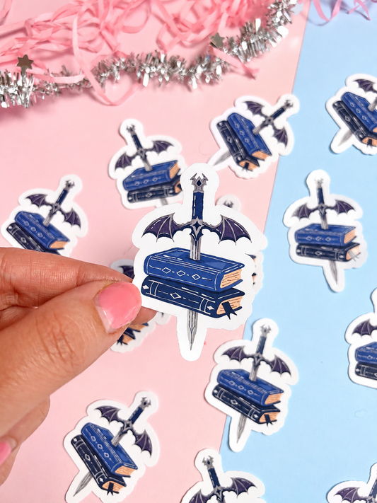 Sword and wings book stack sticker, blue and white design held by hand
