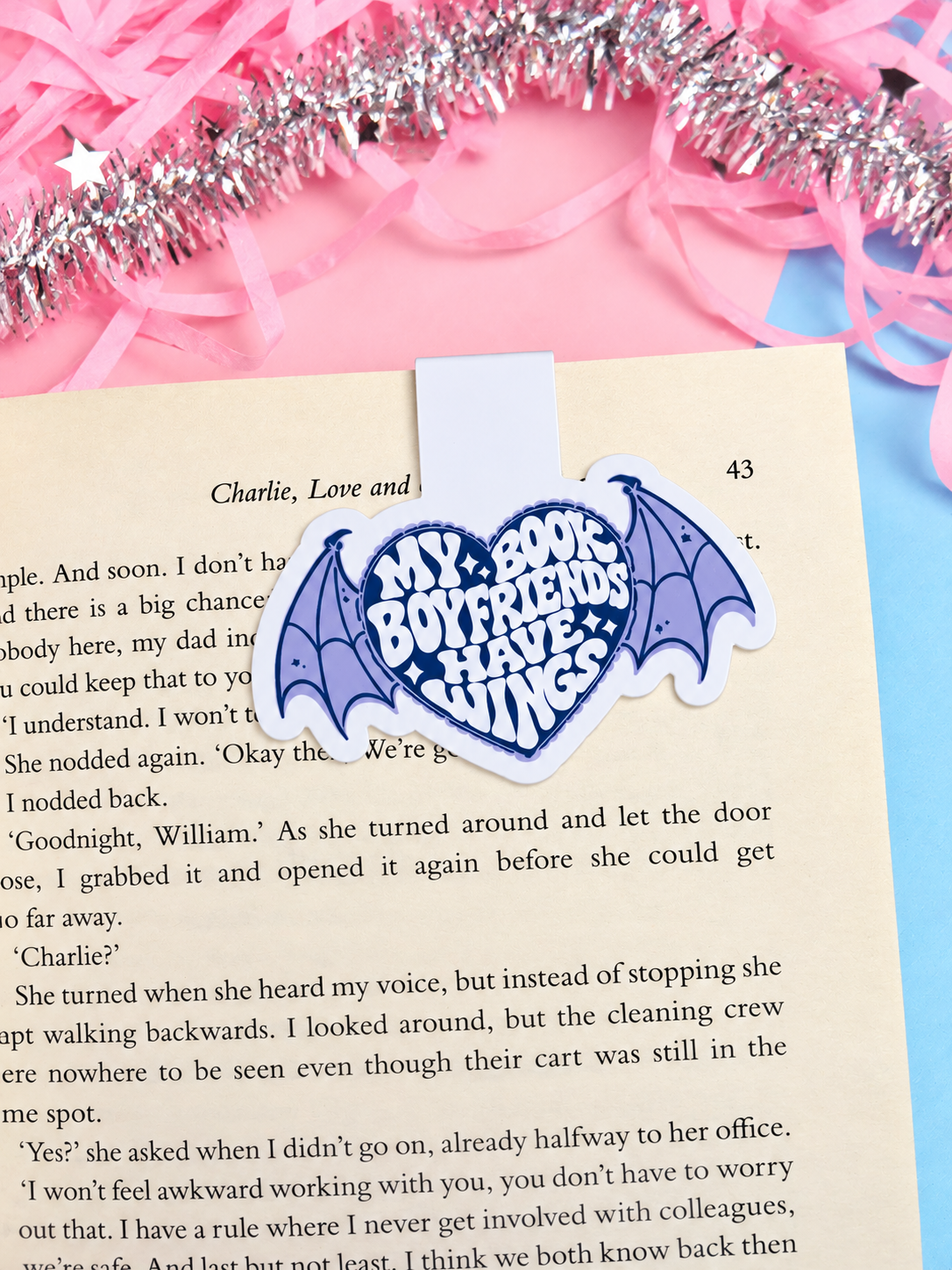 Magnetic bookmark attached to an open book page, featuring a blue winged heart emblem.