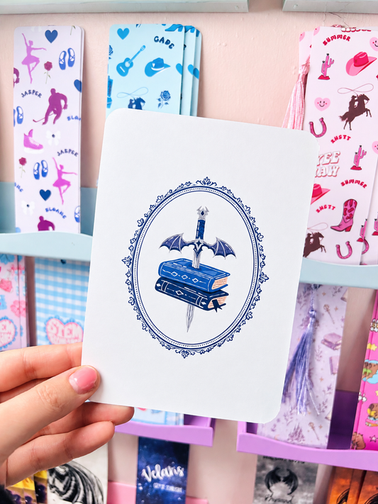 White Kindle insert card held by hand, oval sword-and-books illustration with blue border