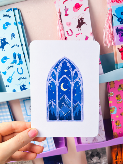 White card insert held in hand with blue arched window, moon and mountain illustration.