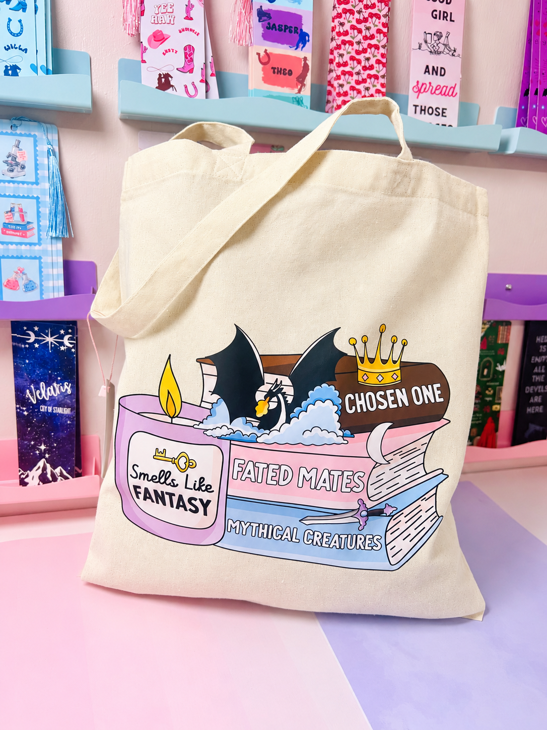 Cream cotton tote bag with fantasy book stack graphic, wide handles.