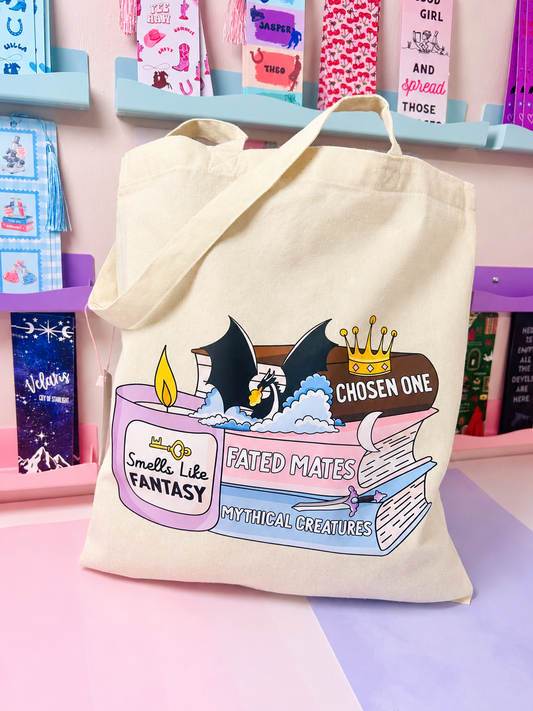 Cream cotton tote bag with fantasy book stack graphic, wide handles.