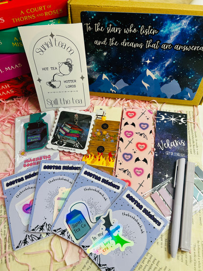 Flat lay of an ACOTAR-themed mystery bookish bundle featuring double-sided bookmarks, holographic stickers, a keyring, art print, annotate tabs, pen and highlighter. Items are displayed with Sarah J. Maas books and pink shredded paper, creating a cosy, fantasy-inspired aesthetic.