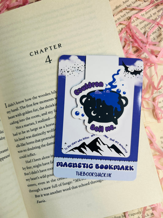Magnetic bookmark featuring a cute bubbling cauldron with the text “Cauldron Boil Me,” clipped to an open book, with pink shredded paper background.


