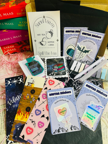 Flat lay of an ACOTAR-themed mystery bookish bundle featuring double-sided bookmarks, holographic stickers, a keyring, art print, annotate tabs, pen and highlighter. Items are displayed with Sarah J. Maas books and pink shredded paper, creating a cosy, fantasy-inspired aesthetic.