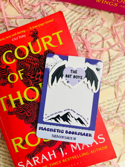 Magnetic bookmark featuring a purple heart with the text “The Bat Boys,” flanked by bat wings, clipped to an open fantasy book.