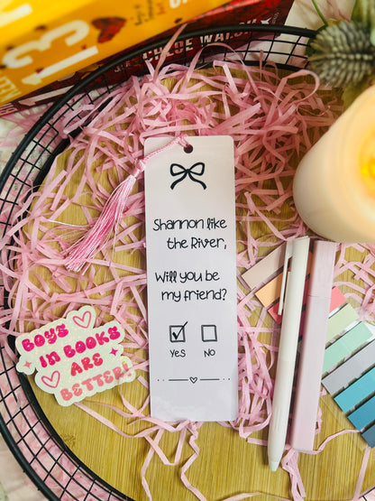 Two pink gingham bookmarks inspired by Binding 13, featuring a friendship note design with the phrase “Shannon like the River, Will you be my friend?” on one and a pink bow pattern on the other, styled with soft bookish decor.