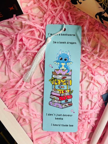This updated bookmark now includes a delicate white tassel, adding a touch of elegance to the charming design. The whimsical dragon sitting atop a vibrant stack of books remains the focal point, paired with the playful quote: “I’m not a bookworm, I’m a book dragon. I don’t just devour books, I hoard them too.” The white tassel complements the light blue background, enhancing its appeal while maintaining functionality for avid readers