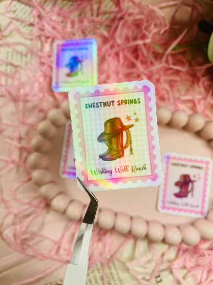 Holographic stamp-style sticker featuring a cowboy hat, lasso, and boots with the text "Chestnut Springs - Wishing Well Ranch" on a pastel gingham background.