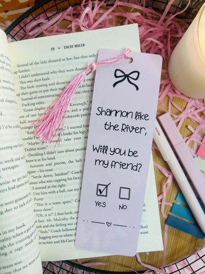 Two pink gingham bookmarks inspired by Binding 13, featuring a friendship note design with the phrase “Shannon like the River, Will you be my friend?” on one and a pink bow pattern on the other, styled with soft bookish decor.