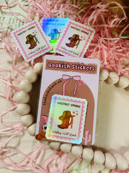 Holographic stamp-style sticker featuring a cowboy hat, lasso, and boots with the text "Chestnut Springs - Wishing Well Ranch" on a pastel gingham background.