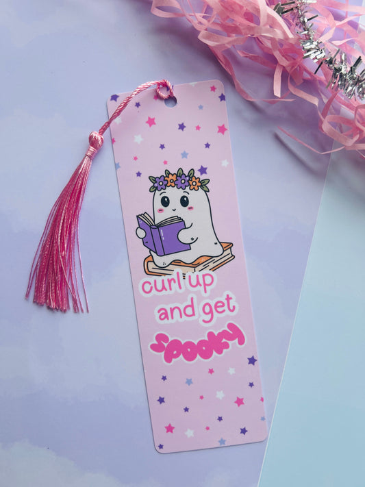 Bookmark with cartoon ghost reading a book, surrounded by stars on a light purple background.