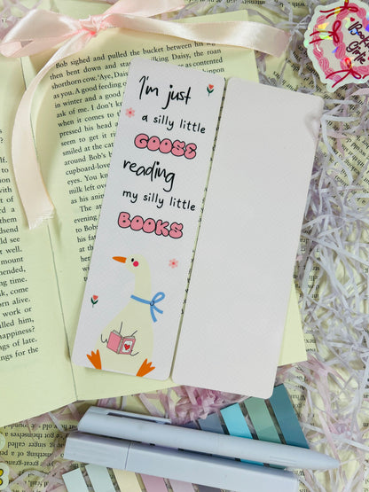 Set of three pastel bookmarks with silly goose and bow designs, placed on an open book with soft pink ribbon, shredded filler, and pens.