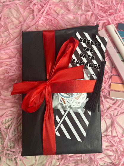 gift wrapped dark romance book with black tissue paper and tied with a red ribbon. Comes with a dark romance bookmark with tassel and pack of mini bookish stickers.
