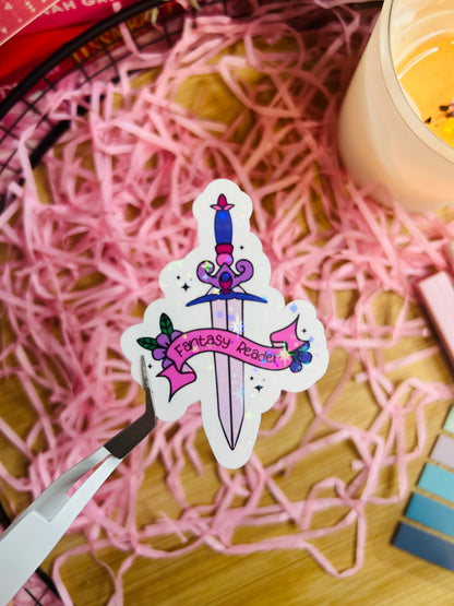 Holographic "Fantasy Reader" sword sticker with a pink and purple design, featuring a decorative sword wrapped in a ribbon banner. Perfect for book lovers and fantasy fans.