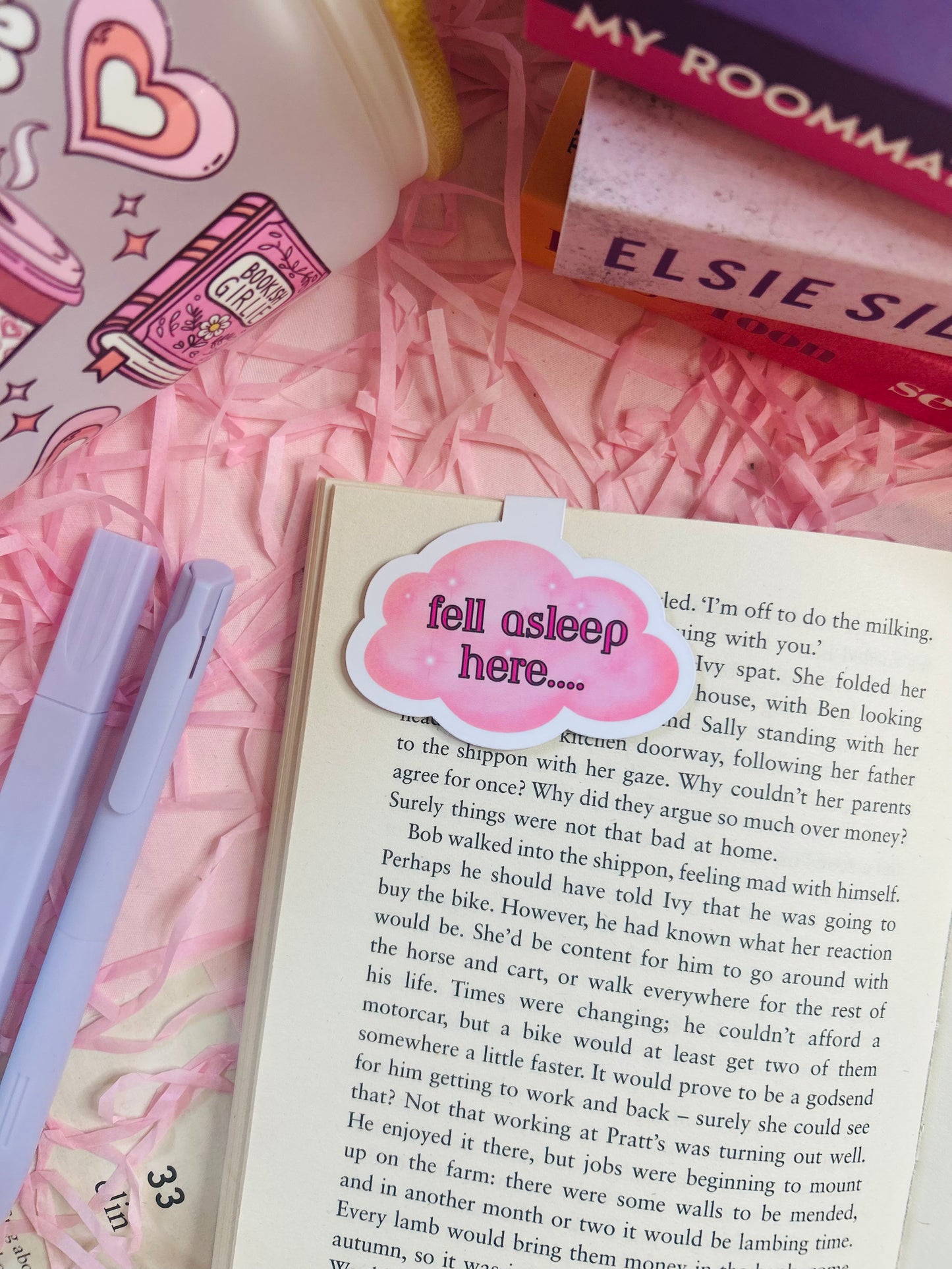 Cloud-shaped magnetic bookmark with the phrase ‘Fell Asleep Here...’ on soft pastel packaging, styled on an open book with cosy pink surroundings.