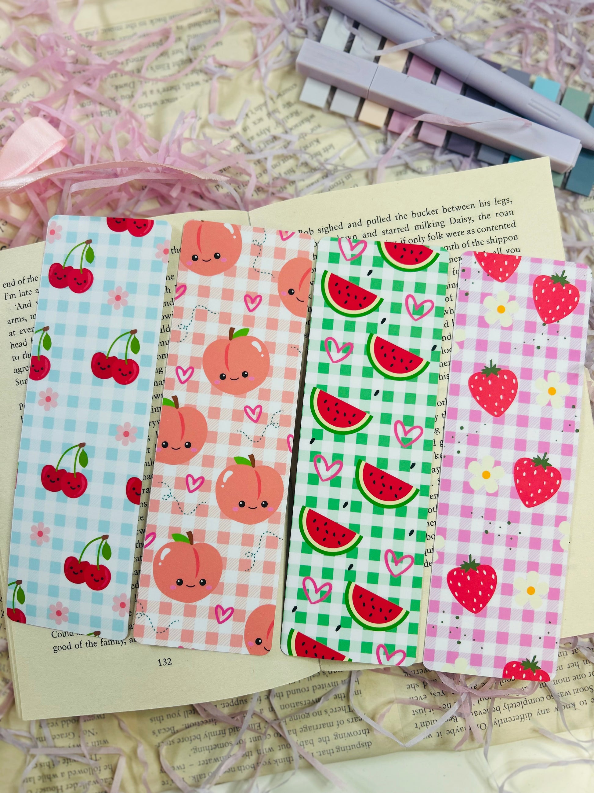 Set of colorful gingham bookmarks with fruit illustrations including cherries, strawberries, and citrus, placed on an open book.